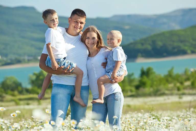 mom, dad, and two sons smiling in a field near a river in troy