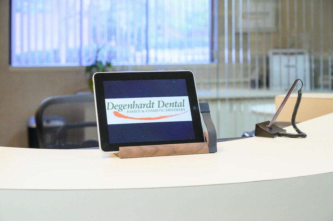 Tablet with degenhardt dental logo rests on white desk with pen nearby